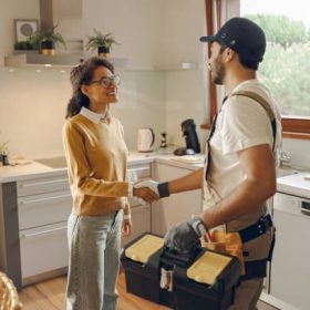 Professional male handyman shaking hands with happy female client while standing at home kitchen